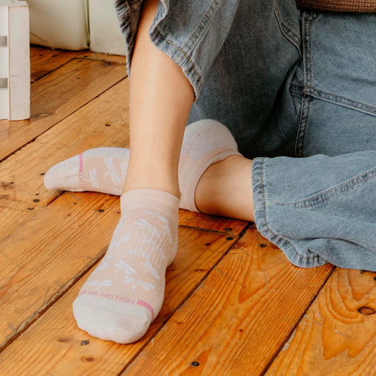 Person wearing light-colored ankle compression socks with a subtle pattern on a wooden floor.