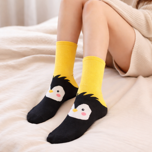 Yellow and black penguin crew socks worn by a person sitting on a beige surface.
