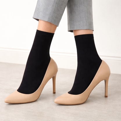 Beige high-heeled shoes with black trouser sock-like covers worn by a person in gray pants.
