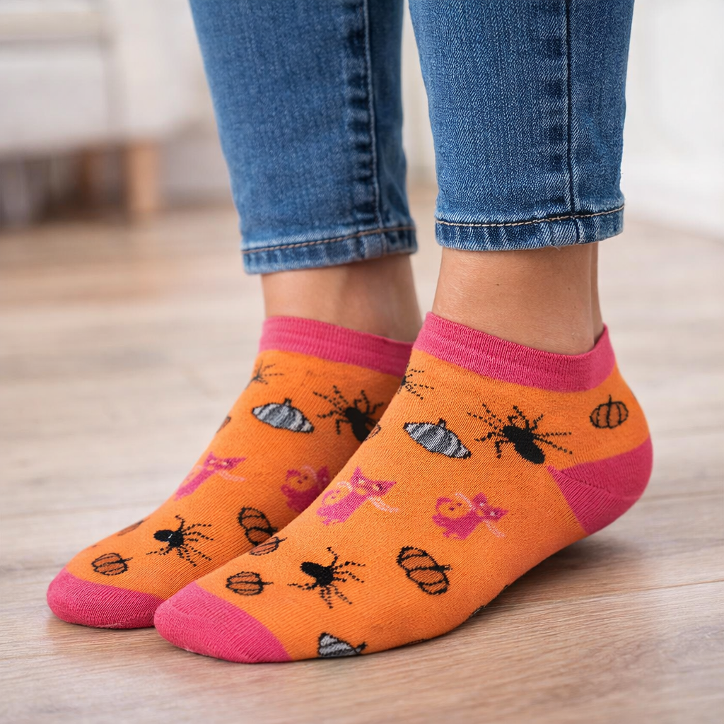Orange Ankle Halloween socks with insect patterns and pink toes worn with blue jeans on a wooden floor.